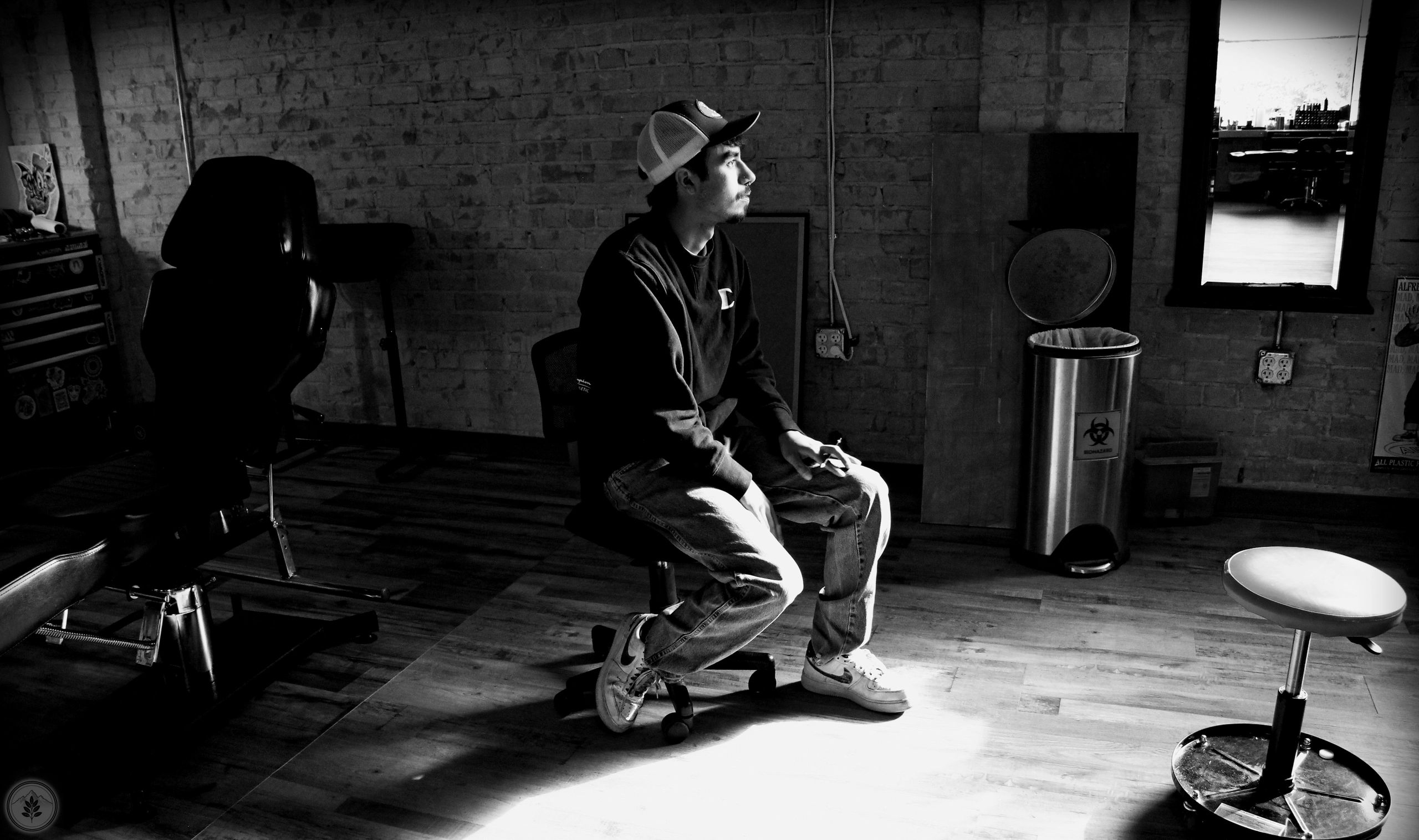 A man sits thoughtfully in a dimly lit room with brick walls.