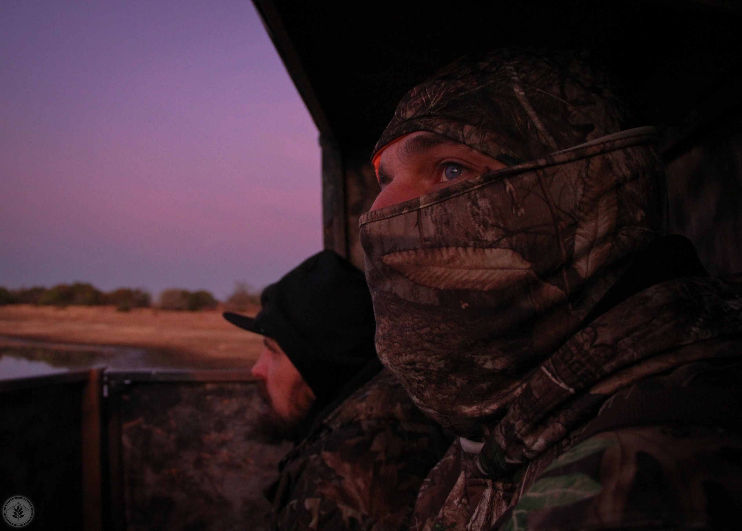 Two camouflaged hunters watching the landscape during twilight.