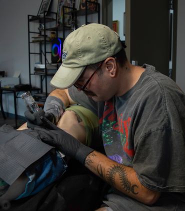 Tattoo artist inking a client’s leg.