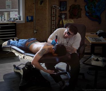 Tattoo artist working on a client's back in a studio.