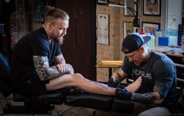 Tattoo artist working on a client's leg tattoo.