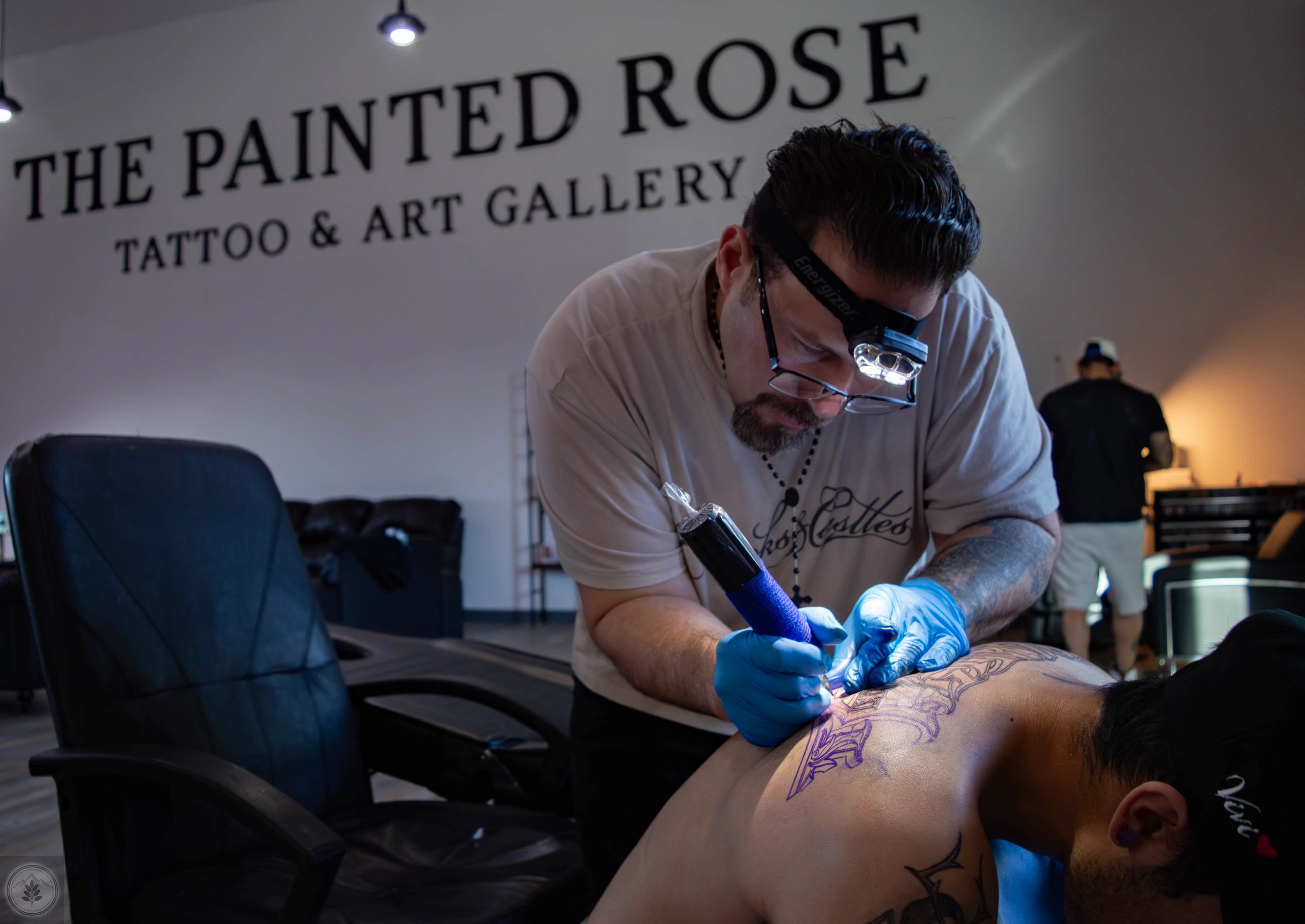 Tattoo artist working on a client's back tattoo at The Painted Rose studio.