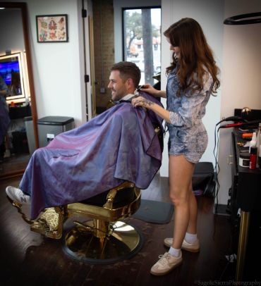 Man getting a haircut from a woman in a barbershop.