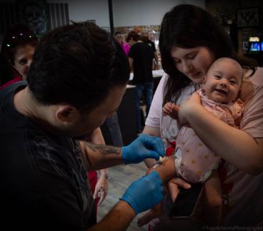 Baby getting a vaccination while smiling in mother's arms.