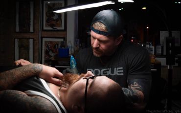 Tattoo artist working on a client's arm in a studio.