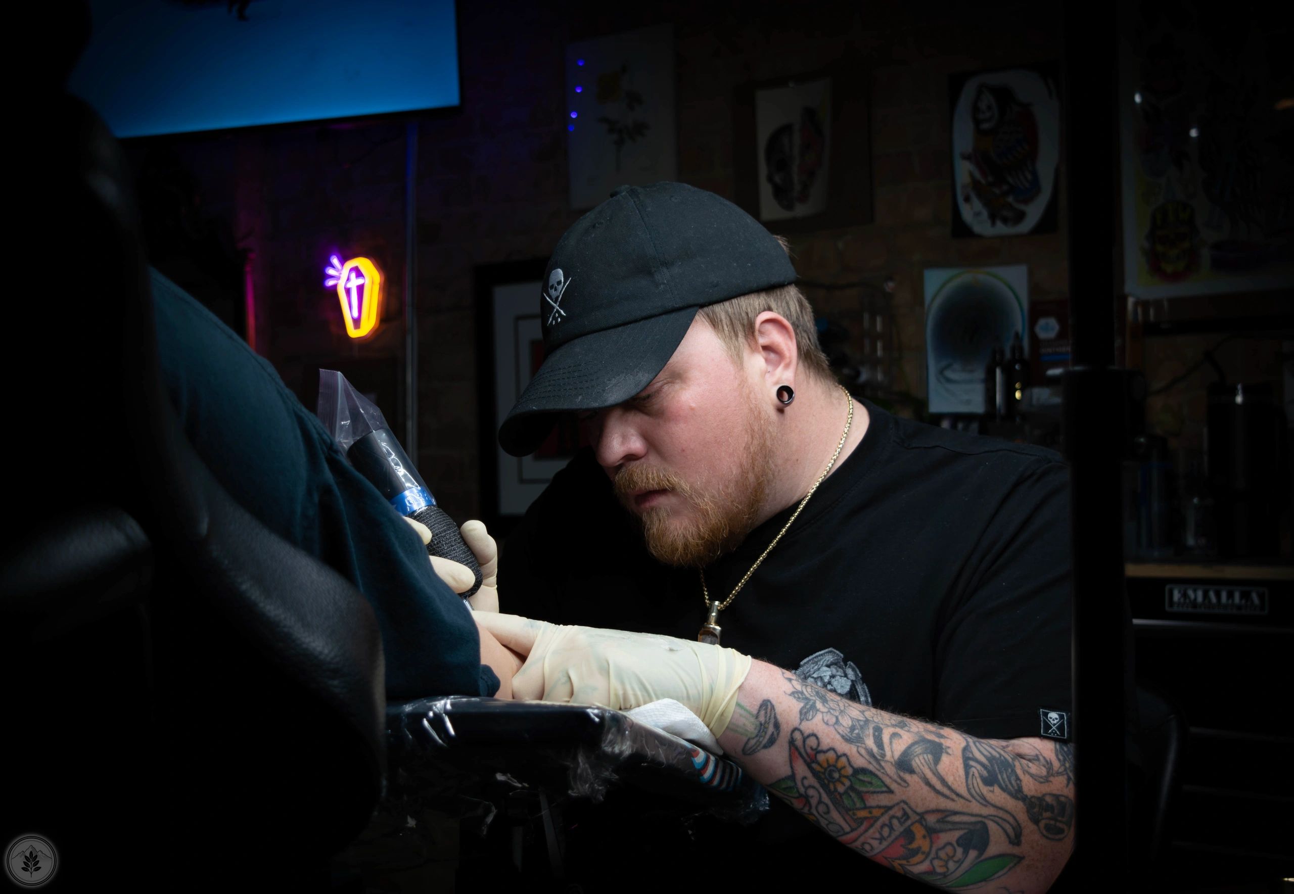 Tattoo artist focused on inking a client's arm in a dimly lit studio.