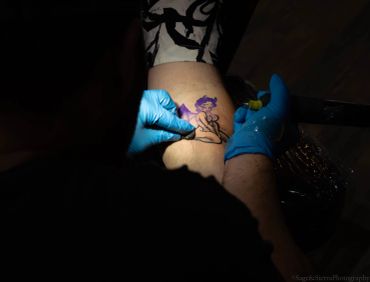 Tattoo artist working on a colorful tattoo on a person's leg.