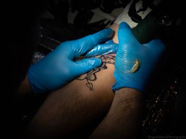Tattoo artist working on a client's arm with blue gloves.