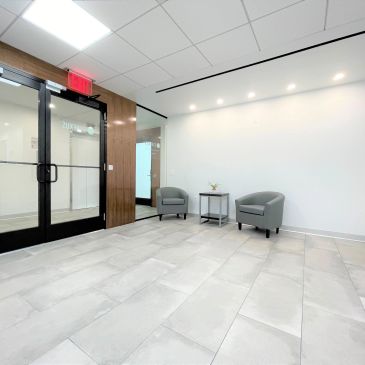 Minimalist waiting area with two gray chairs and a small table against a white wall.