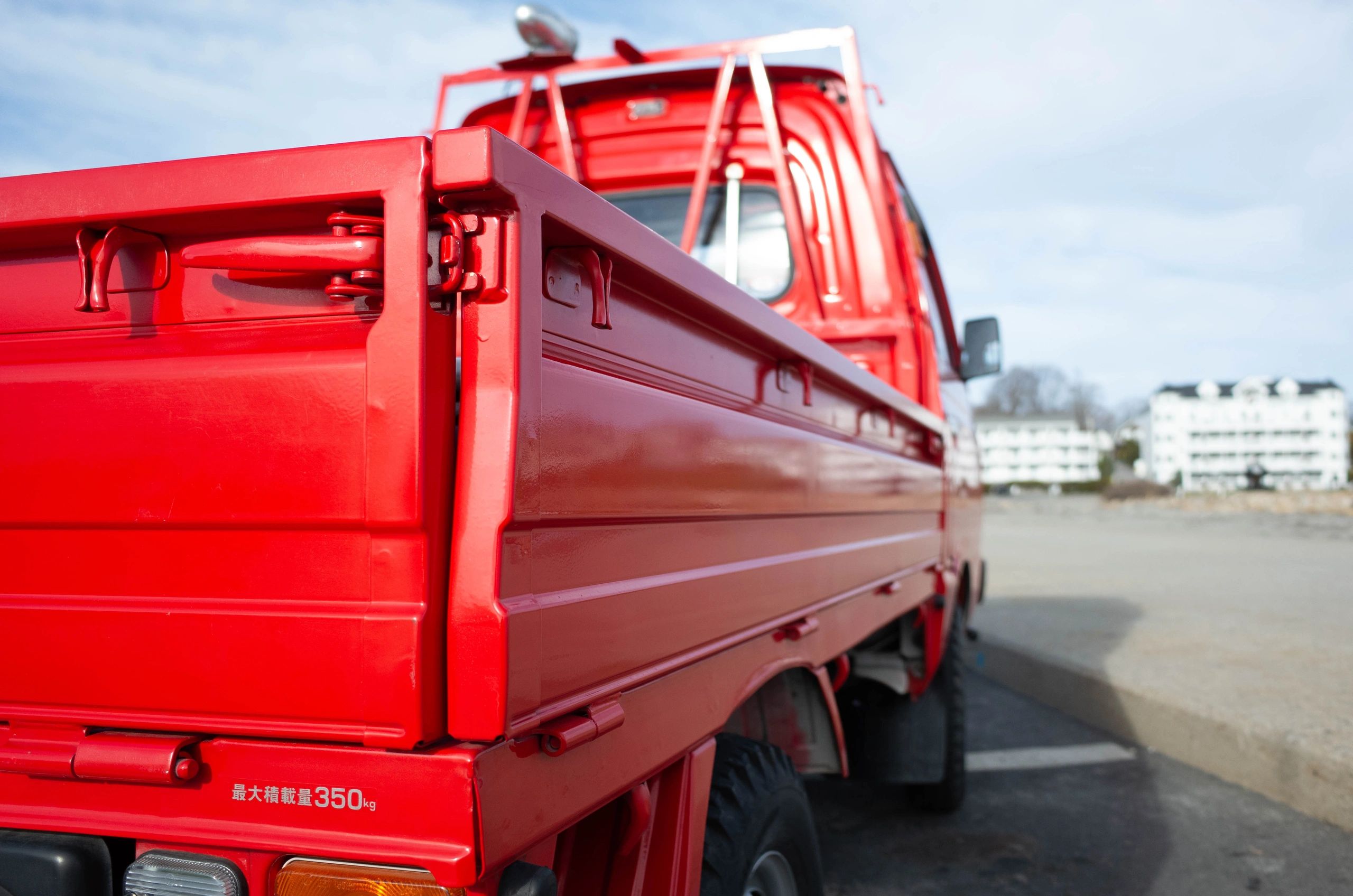 Vibrant red 1987 Subaru Sambar Kei truck on a Maine beach, presented by OIWA.