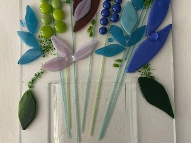 Colorful glass flowers arranged in a clear vase on a white background.