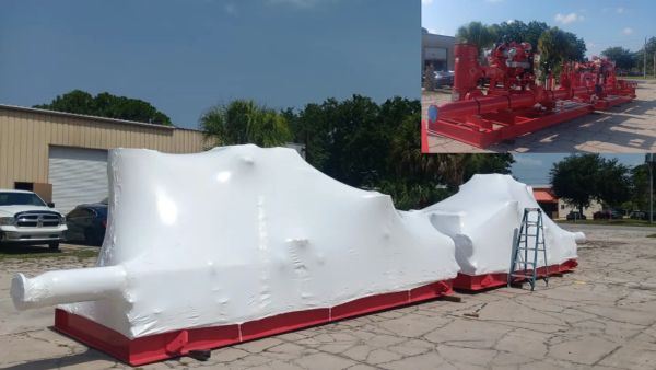 Industrial red machinery covered in white protective shrink wrap outdoors.
