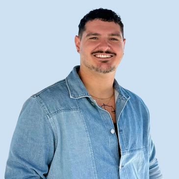 Smiling man in a denim jacket against a light blue background.
