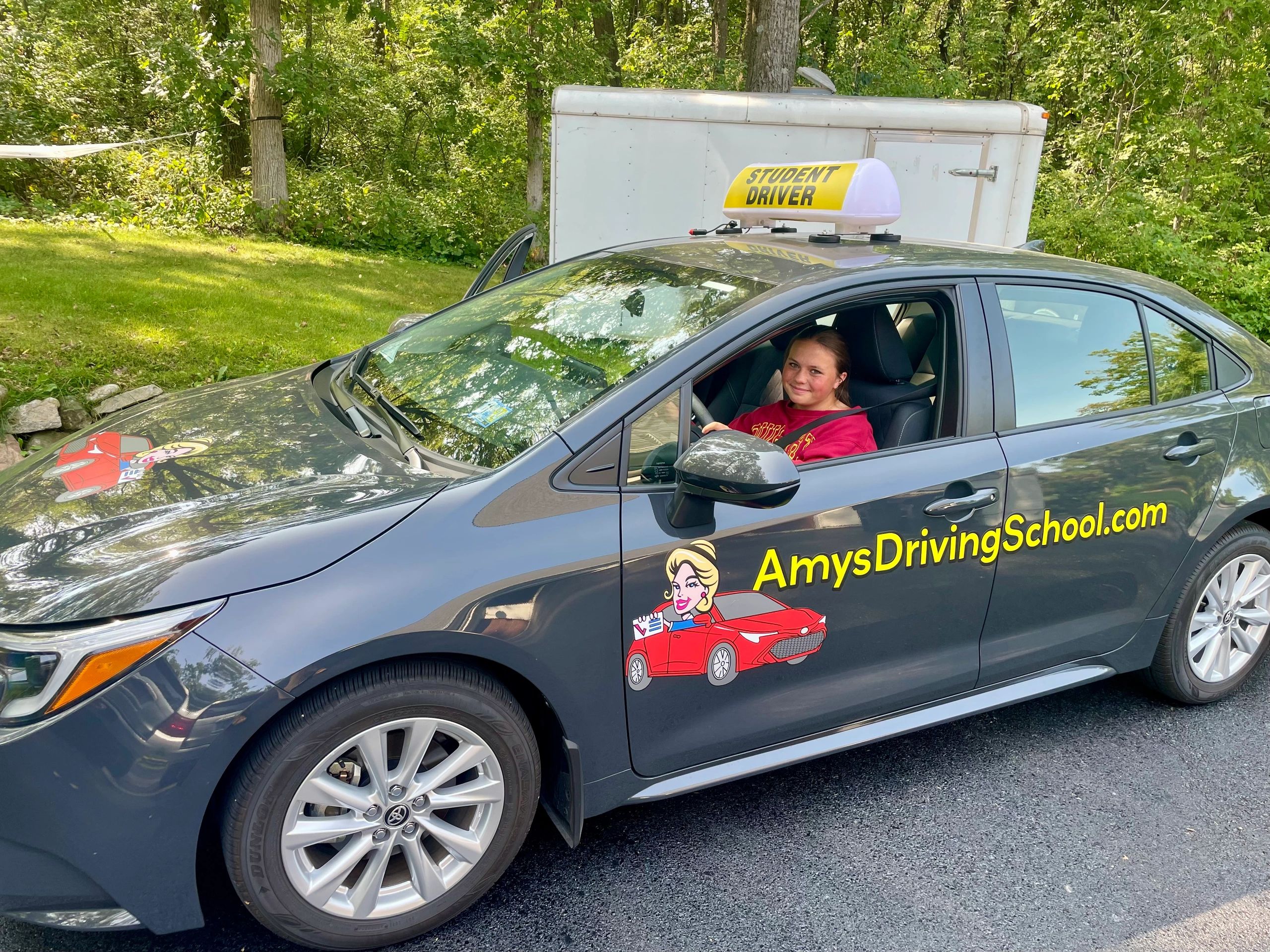 Teen student driver sitting in a driving school car with a sign on top.