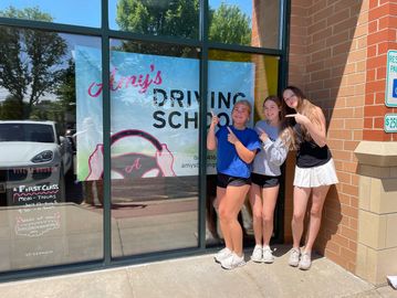 Three young women posing outside a driving school.