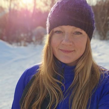 A woman in a blue jacket and black hat outdoors in snowy sunlight.