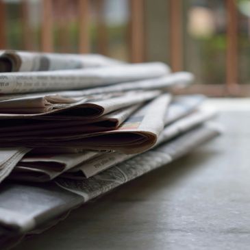 A stack of folded newspapers on a marble surface near a window.