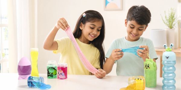 Two kids playing with colorful slime toys at a table.