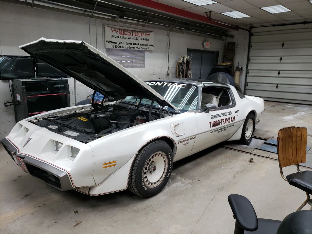 White Pontiac Turbo Trans Am with hood open in a garage.