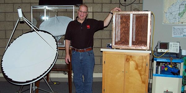 Man standing next to electronics and a large dish antenna.