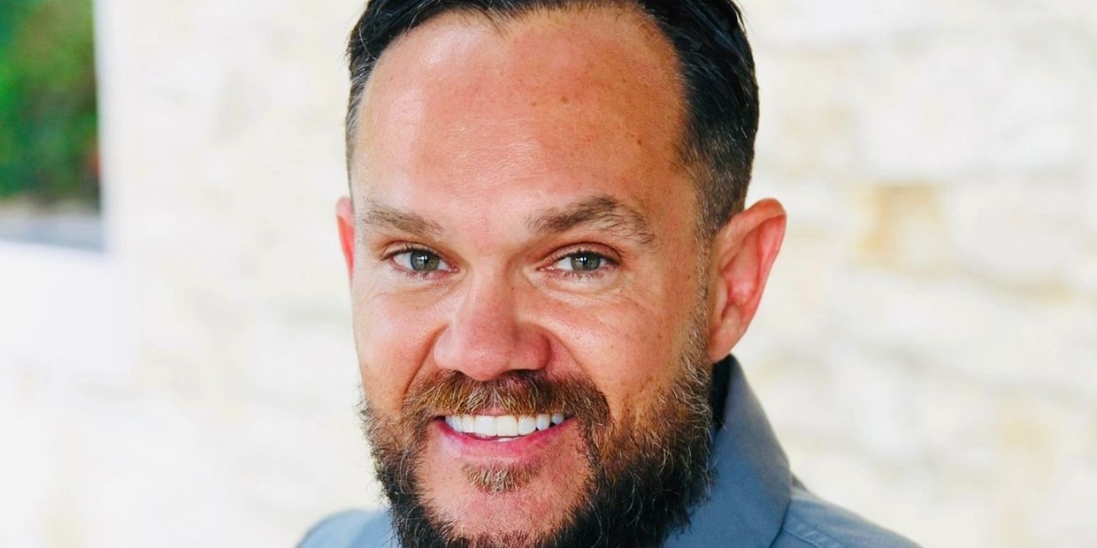 Close-up of a smiling man with a beard and green eyes.