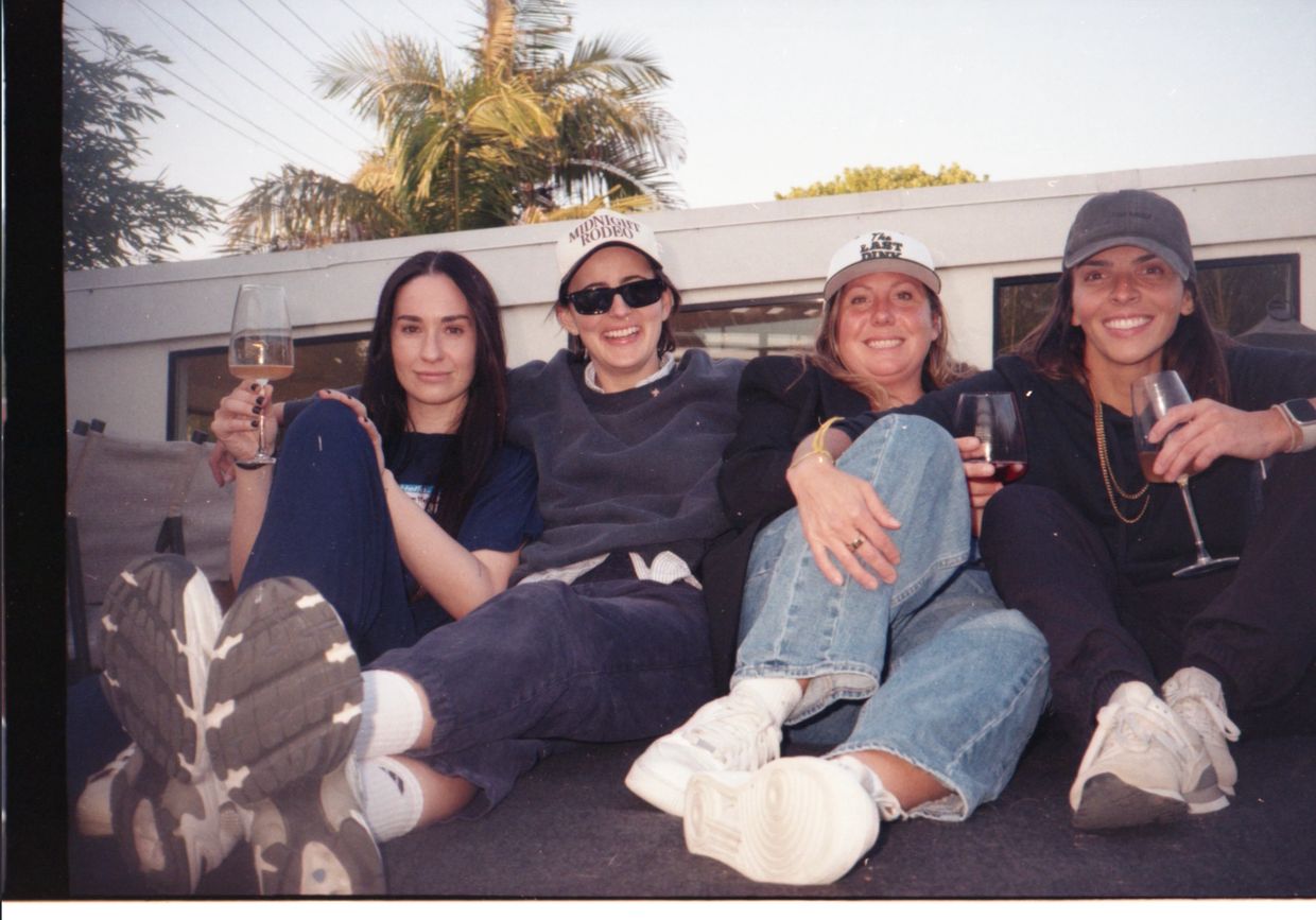 Four friends sitting outdoors on a rooftop, enjoying drinks and wearing casual clothes.