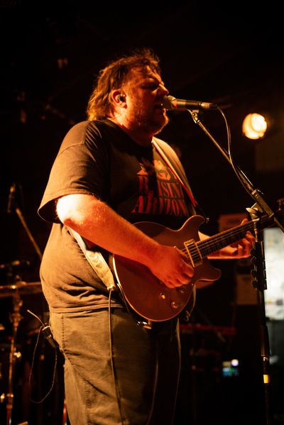 Man singing and playing electric guitar on stage.