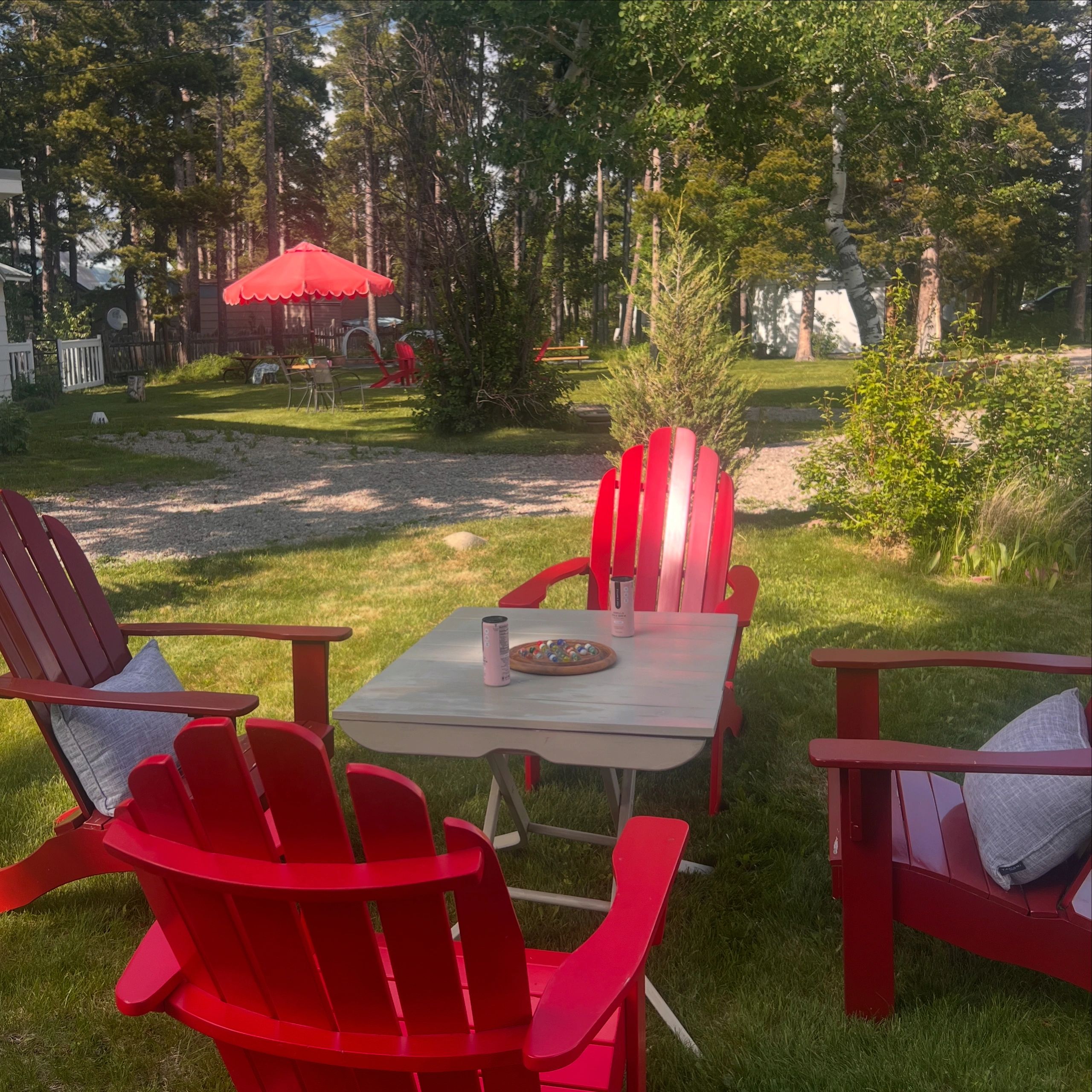 Red adirondack chairs around a game table on a green lawn