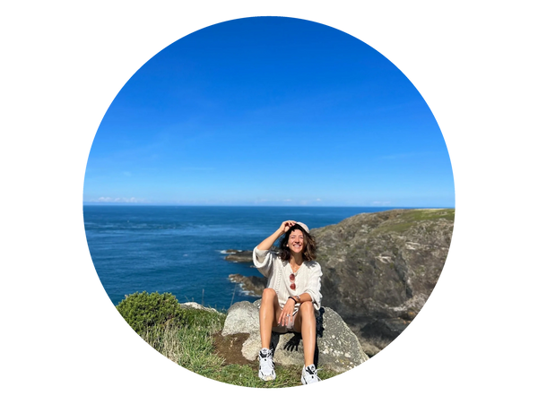 Dana female founder sat on a rock / cliffs at the seaside, smiling looking healthy. blue skies & sea