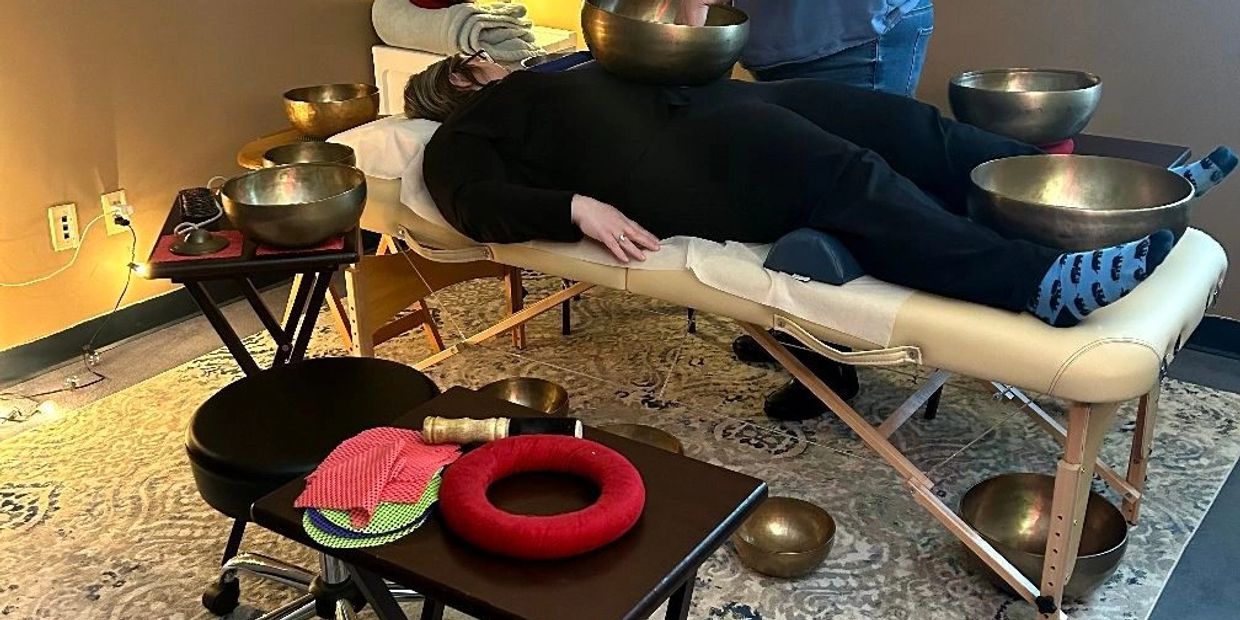 Person lying on a massage table surrounded by singing bowls for sound therapy.