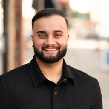 Smiling man with beard and neat haircut wearing a black jacket.
