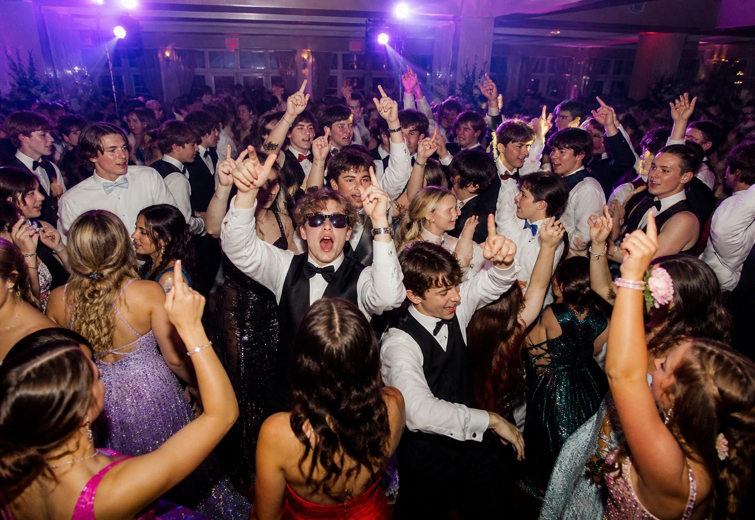 Crowd of young people dancing and celebrating at a formal event.