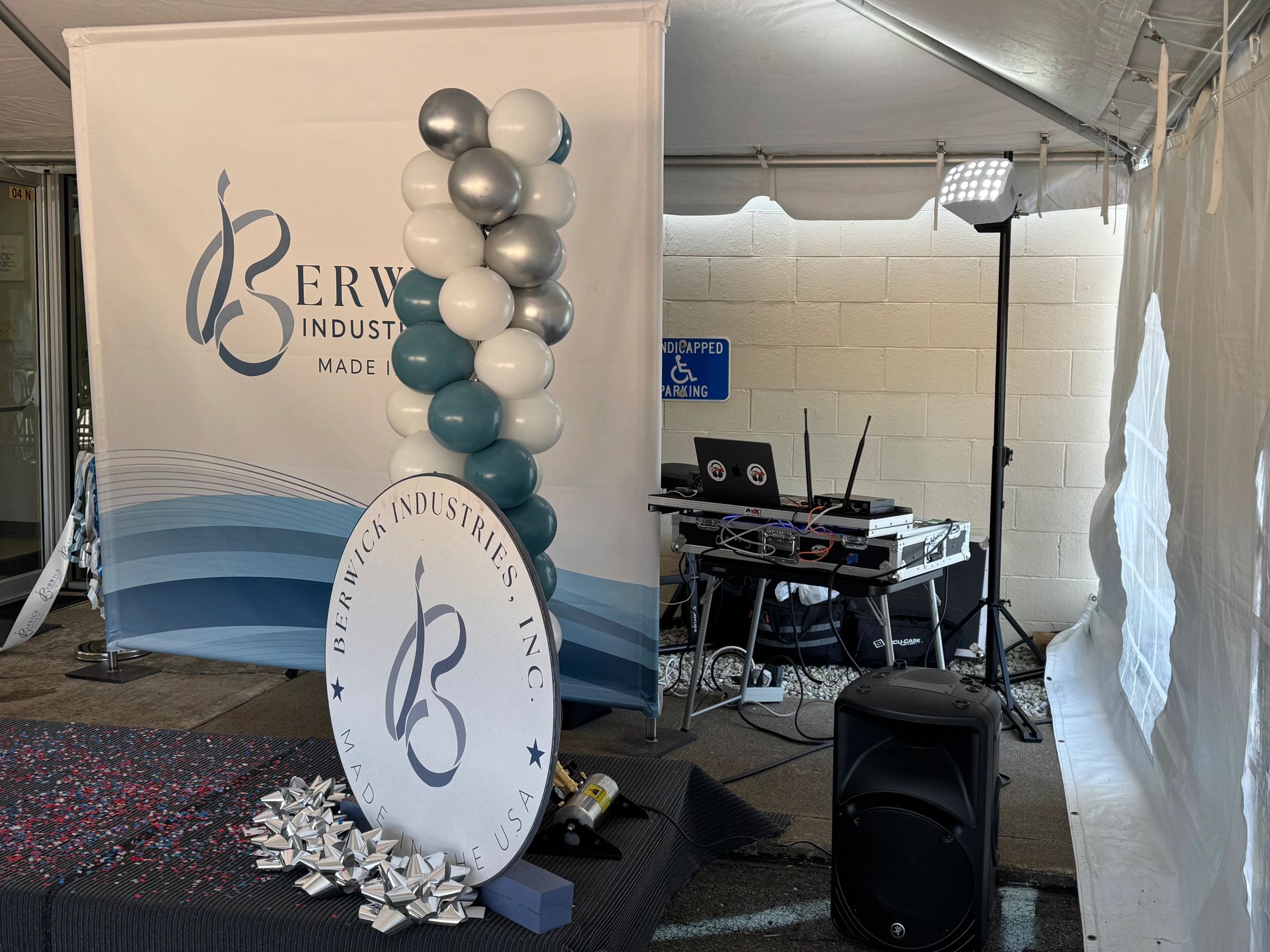 Event setup with balloons, a banner, and DJ equipment under a tent.