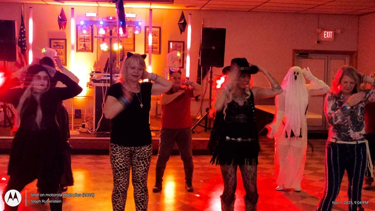 Group of people dancing in Halloween costumes at a party with colorful lights.