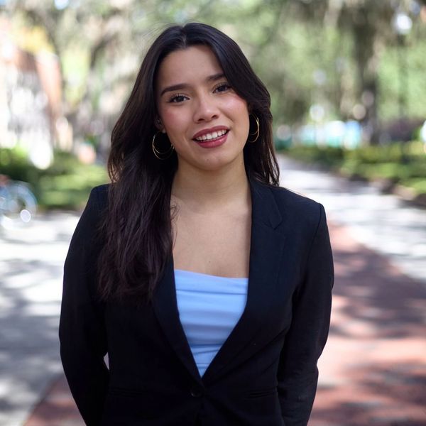 Young woman smiling outdoors wearing a black blazer.
