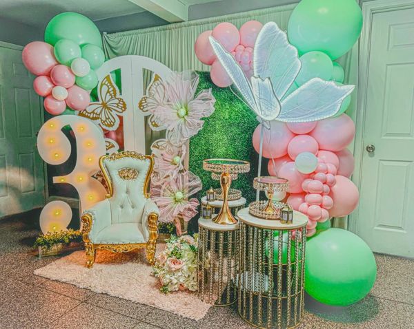 Elegant party setup with a golden chair, pastel balloons, and floral decorations.