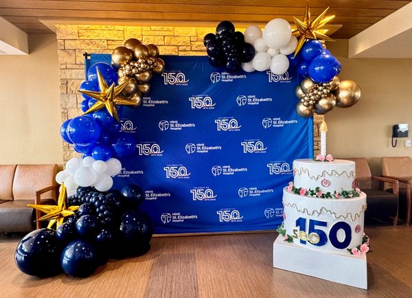 Decorative celebration setup for St. Elizabeth's Hospital's 150th anniversary with balloons and a cake.