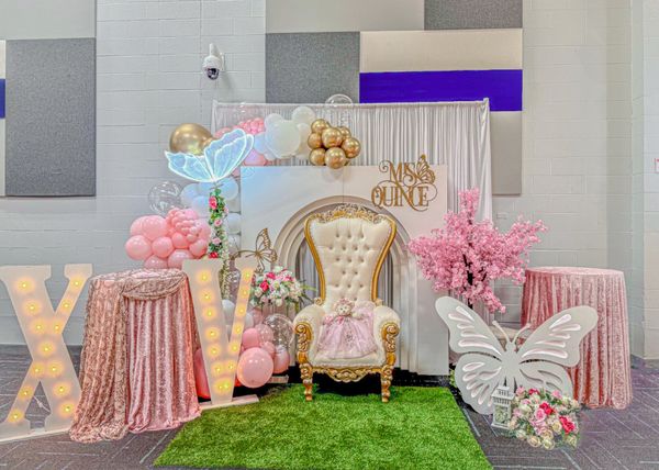 Elegant quinceañera setup with balloons, butterflies, and a royal chair.