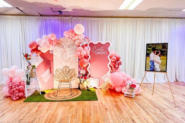 Pink-themed baby shower setup with balloons, flowers, and a photo of a couple.