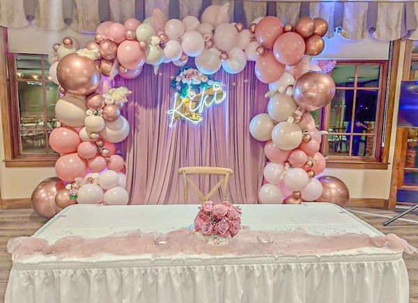 Decorative balloon arch with pink and gold balloons behind a white table with floral centerpiece.