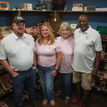 Four people posing together in a cigar shop.