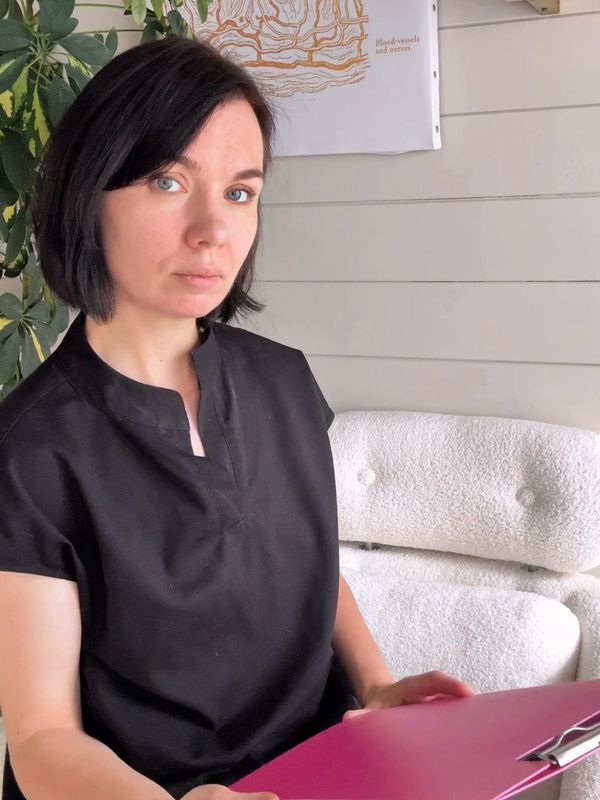 Woman with black hair in black shirt sitting indoors with a pink folder.