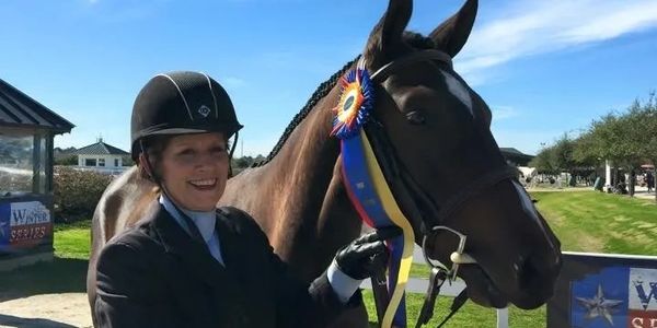 Happy rider holding a horse with a colorful award ribbon on its bridle.
