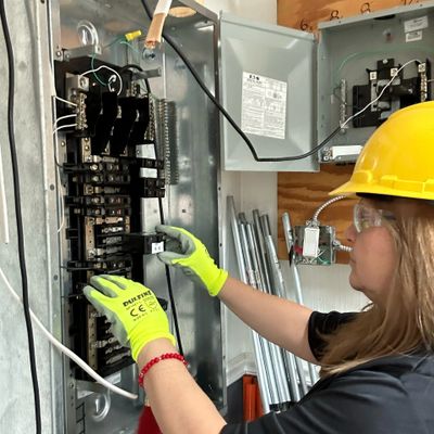 Person wearing safety gear working on an electrical panel inside a control box.