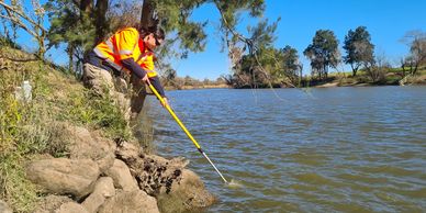 Field tech using sampling pole to  get a water sample from Hunter River