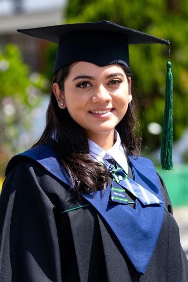 A young woman in a graduation gown and cap smiling outdoors.