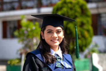Smiling graduate in cap and gown outdoors.