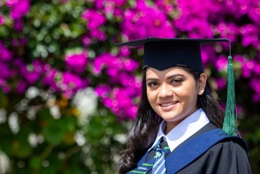 Smiling graduate in cap and gown outdoors.