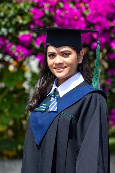 Young woman in graduation gown with a bright floral background.