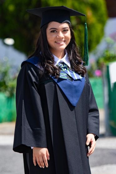 A young woman in graduation gown and cap smiles outdoors.